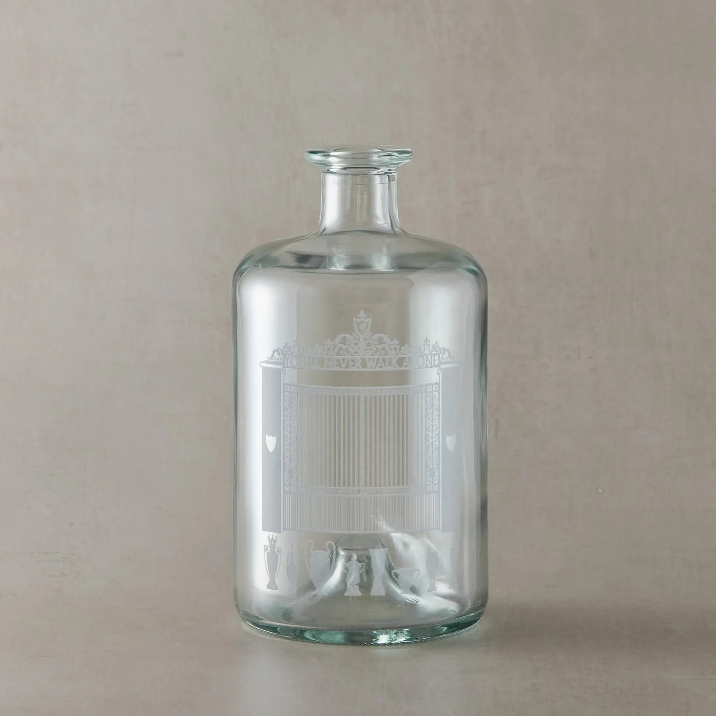 Clear glass bottle with engraved Anfield design on a beige background