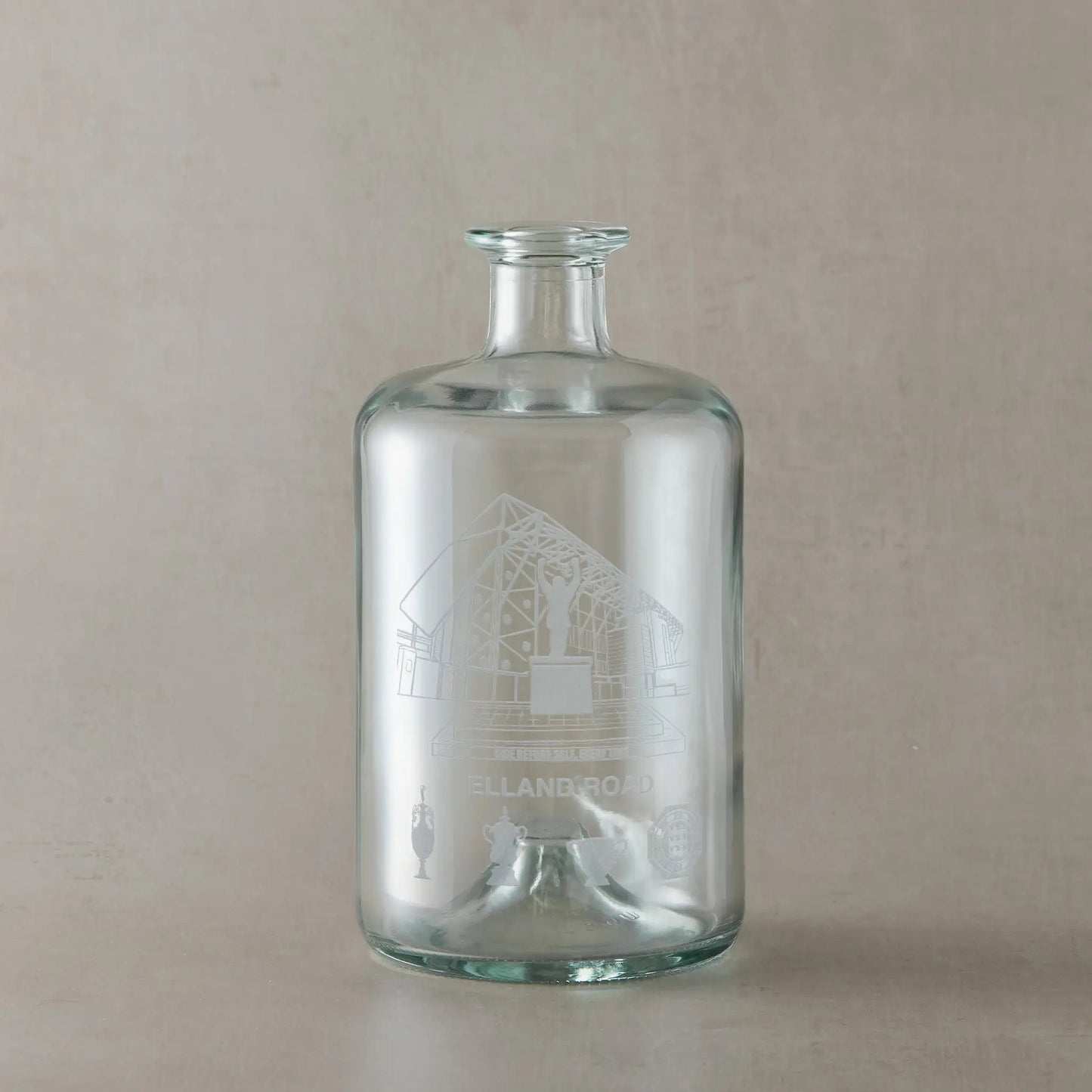 Clear glass bottle with engraved Elland Road design on a beige background