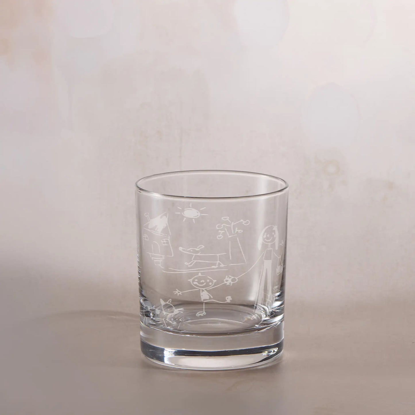 Clear glass tumbler with engraved childs drawing on a beige background