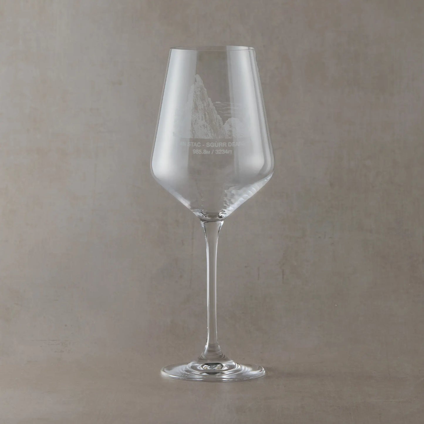 Wine glass with engraved Inaccessible Pinnacle illustration on a beige background