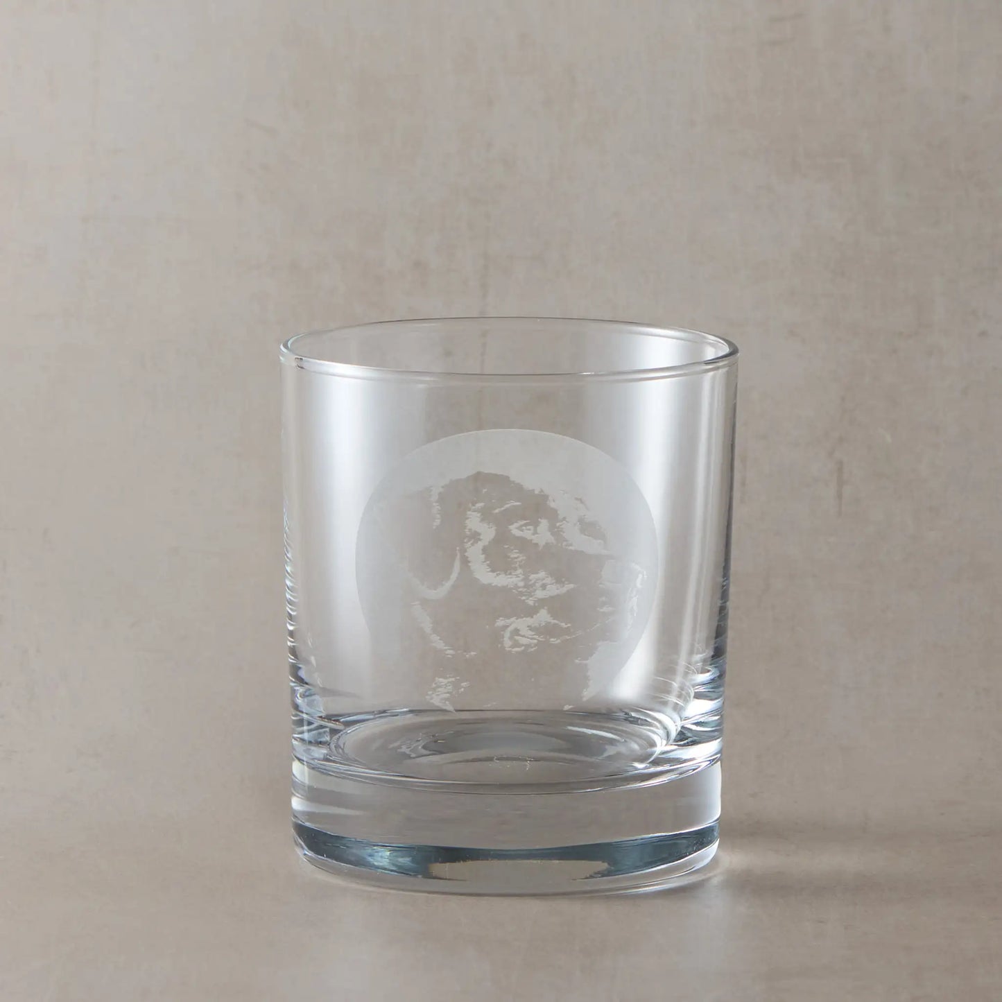 Whisky glass with engraved portrait of a Labrador Retriever on a beige background
