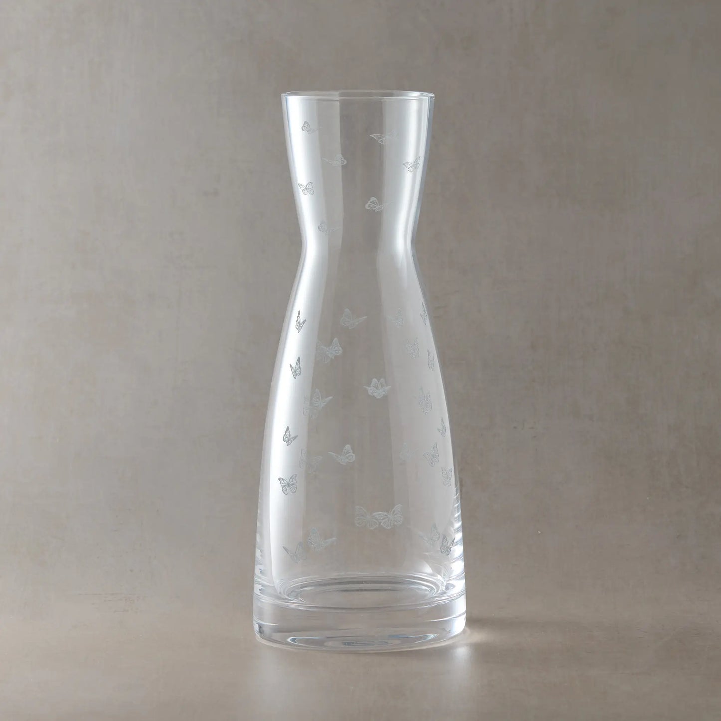 Clear glass carafe with engraved butterfly designs on a beige background