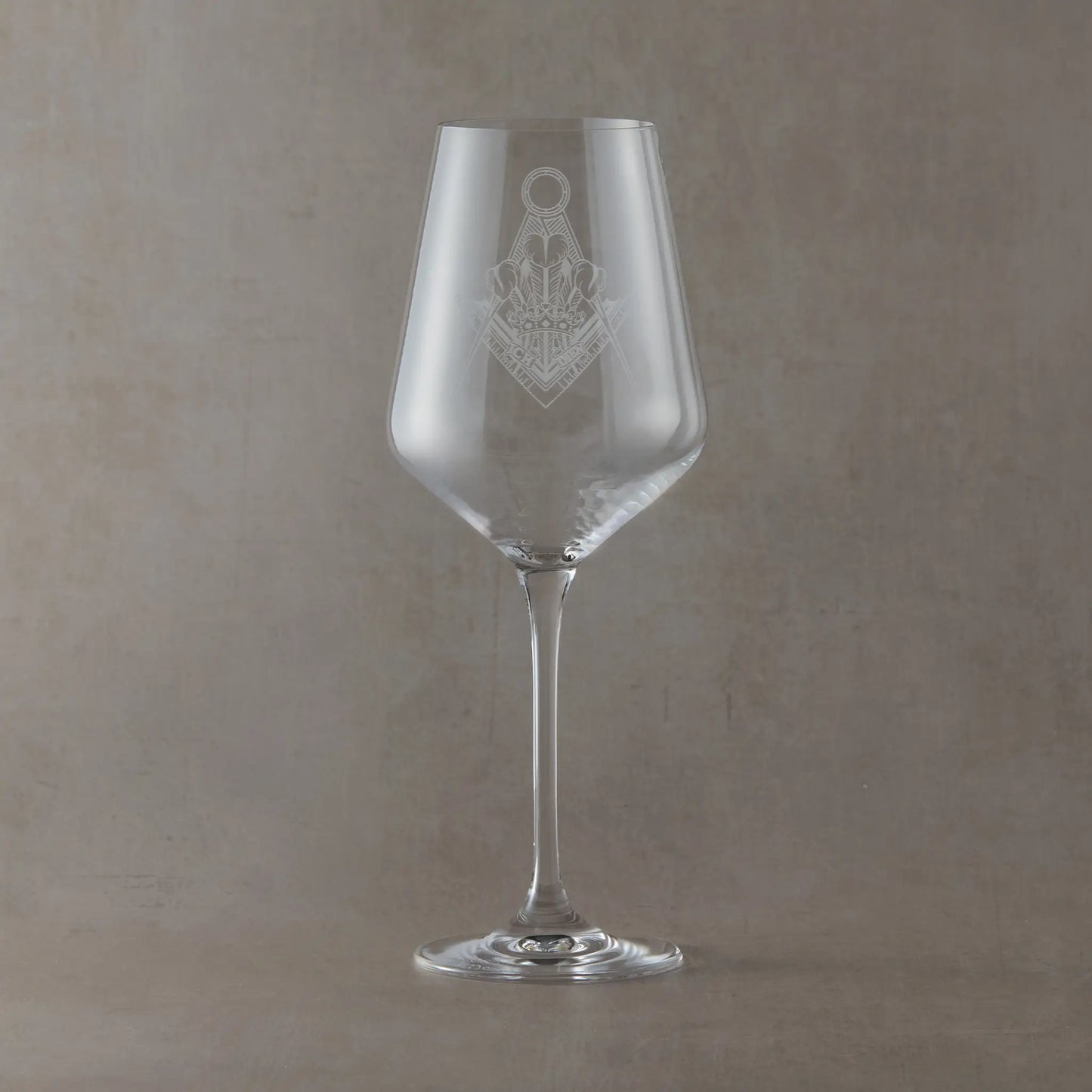 Clear wine glass engraved with a Masonic lodge crest design, shown as an example layout for custom lodge or personal engraving, set on a neutral beige studio background