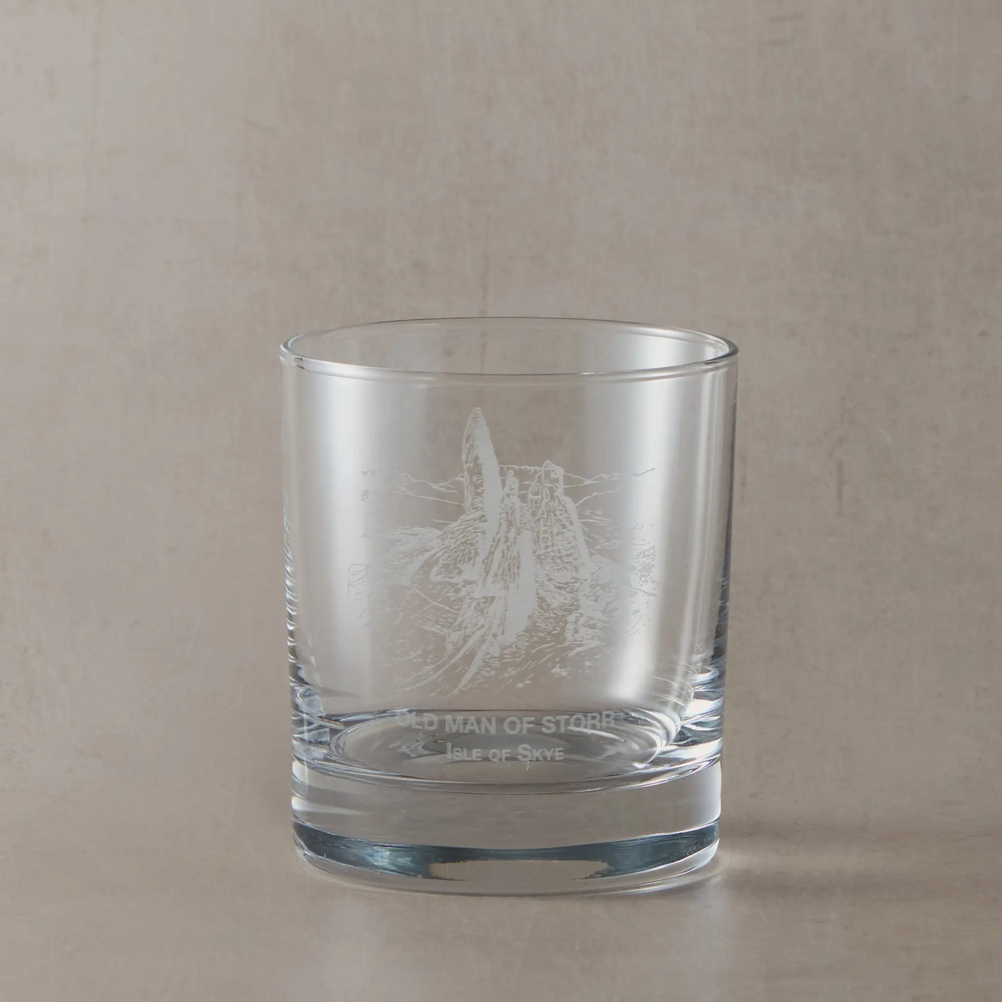 Clear whisky glass engraved with the Old Man of Storr rock formation on a soft neutral beige background