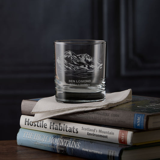 Whisky glass engraved with the mountain Ben Lomond on a stack of books against a dark background