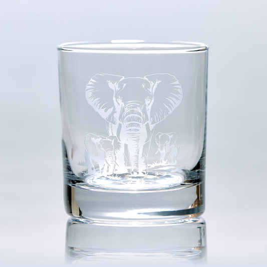 Engraved whisky glass featuring a mother elephant and her two calves, photographed on a white background to show glass clarity and design detail.