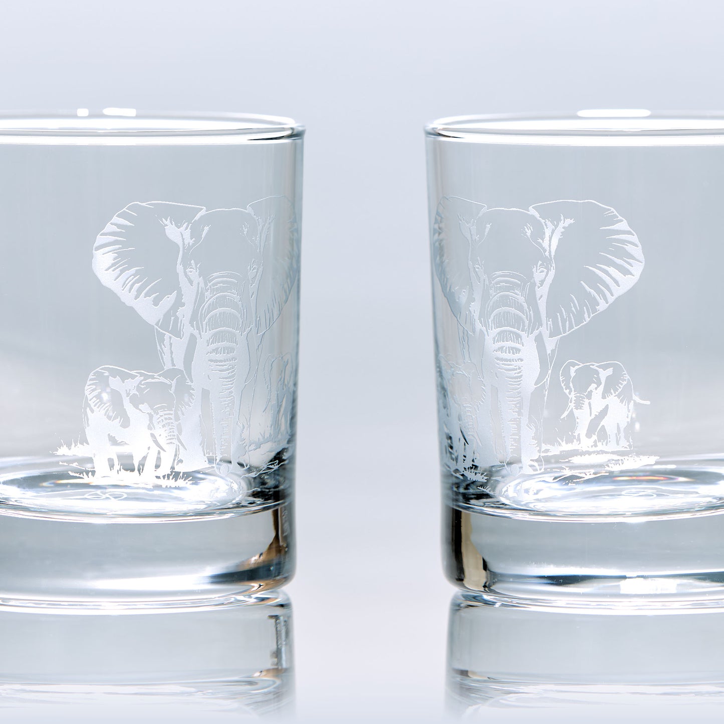 Side view engraved whisky glass featuring a mother elephant and her two calves, photographed on a pale background to show glass clarity and design detail.