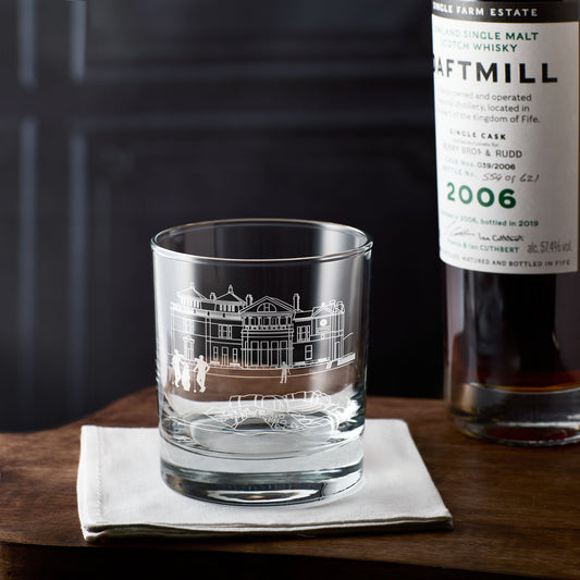 St andrews whisky glass with engraved golf clubhouse design next to a bottle of Daftmill whisky on a wooden surface.