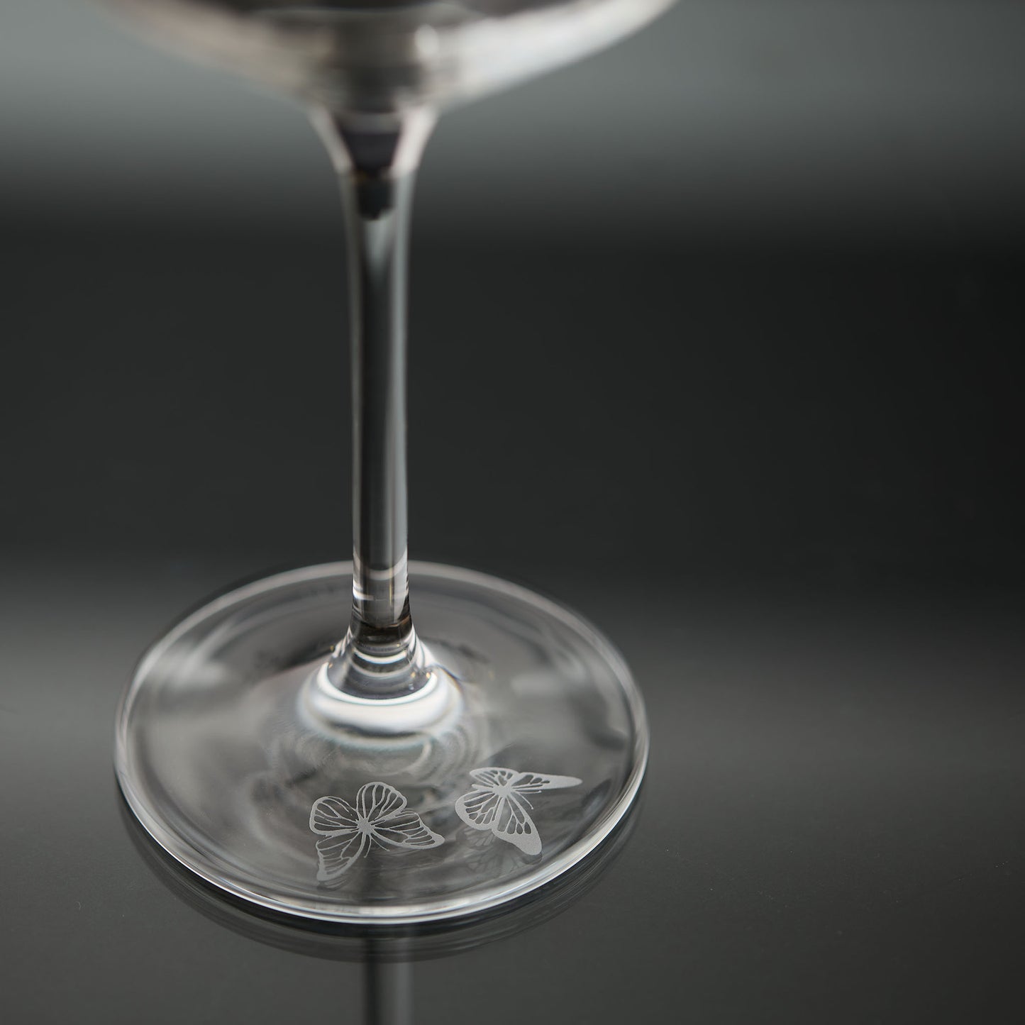 Wine glass with butterfly engraving the foot of the stem on a dark background