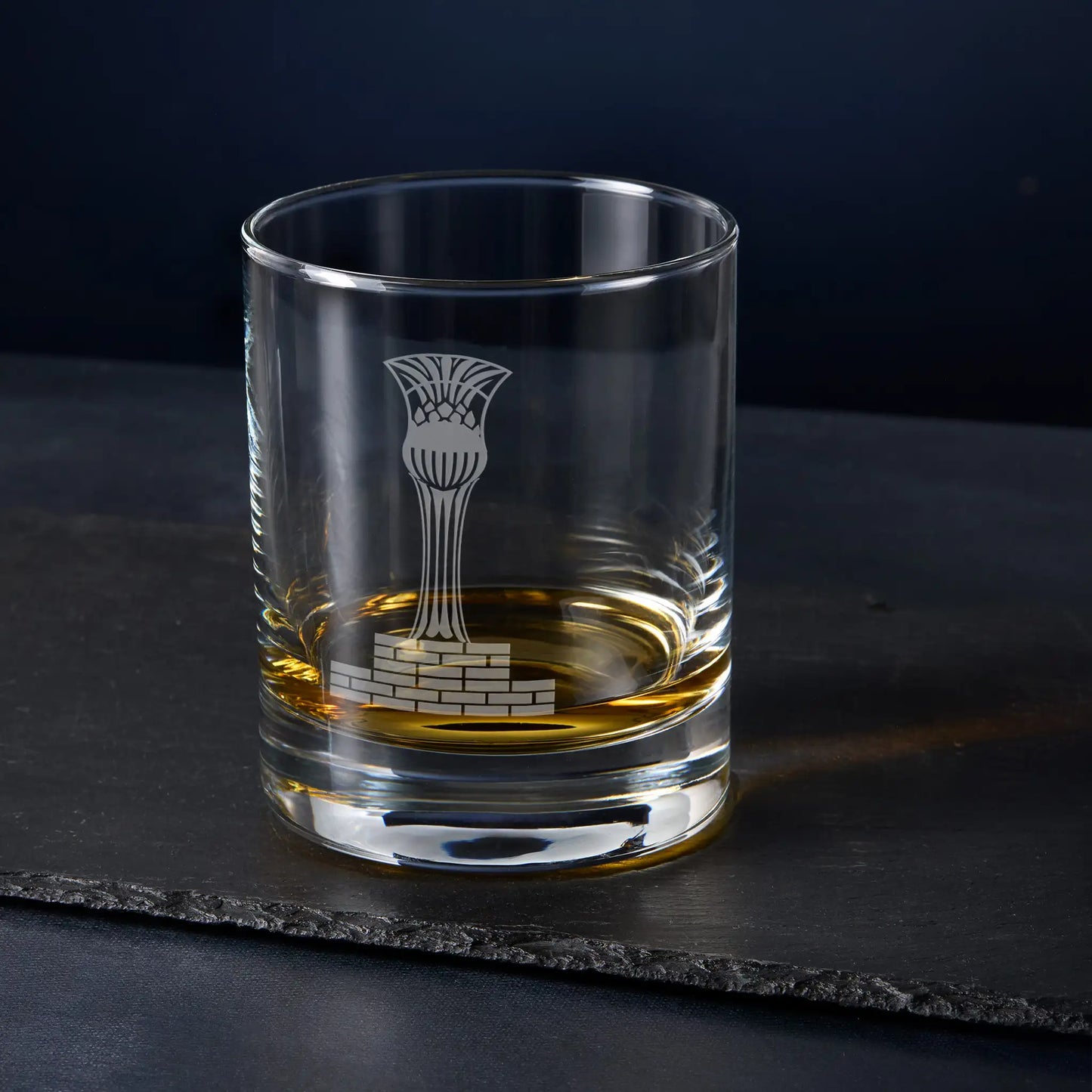 Clear glass tumbler with engraved masonic steward cup design on a dark surface