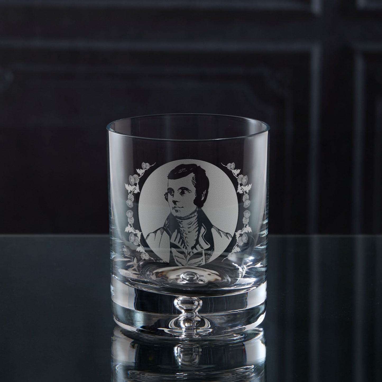 Clear glass tumbler with engraved portrait of the Scottish Poet Rabbie Burns on a dark surface