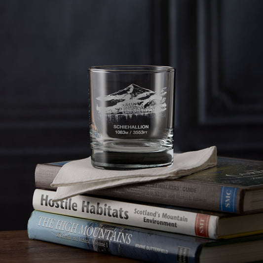 Whisky glass engraved with the Munro Schiehallion on a stack of books against a dark background