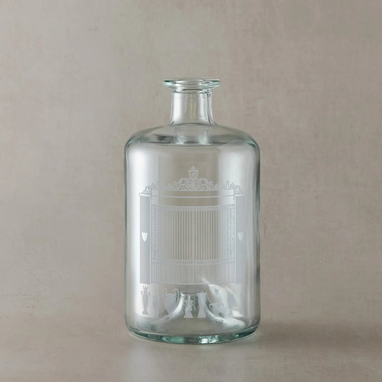 Clear glass bottle with engraved Shankly Gates and trophies design on a beige background