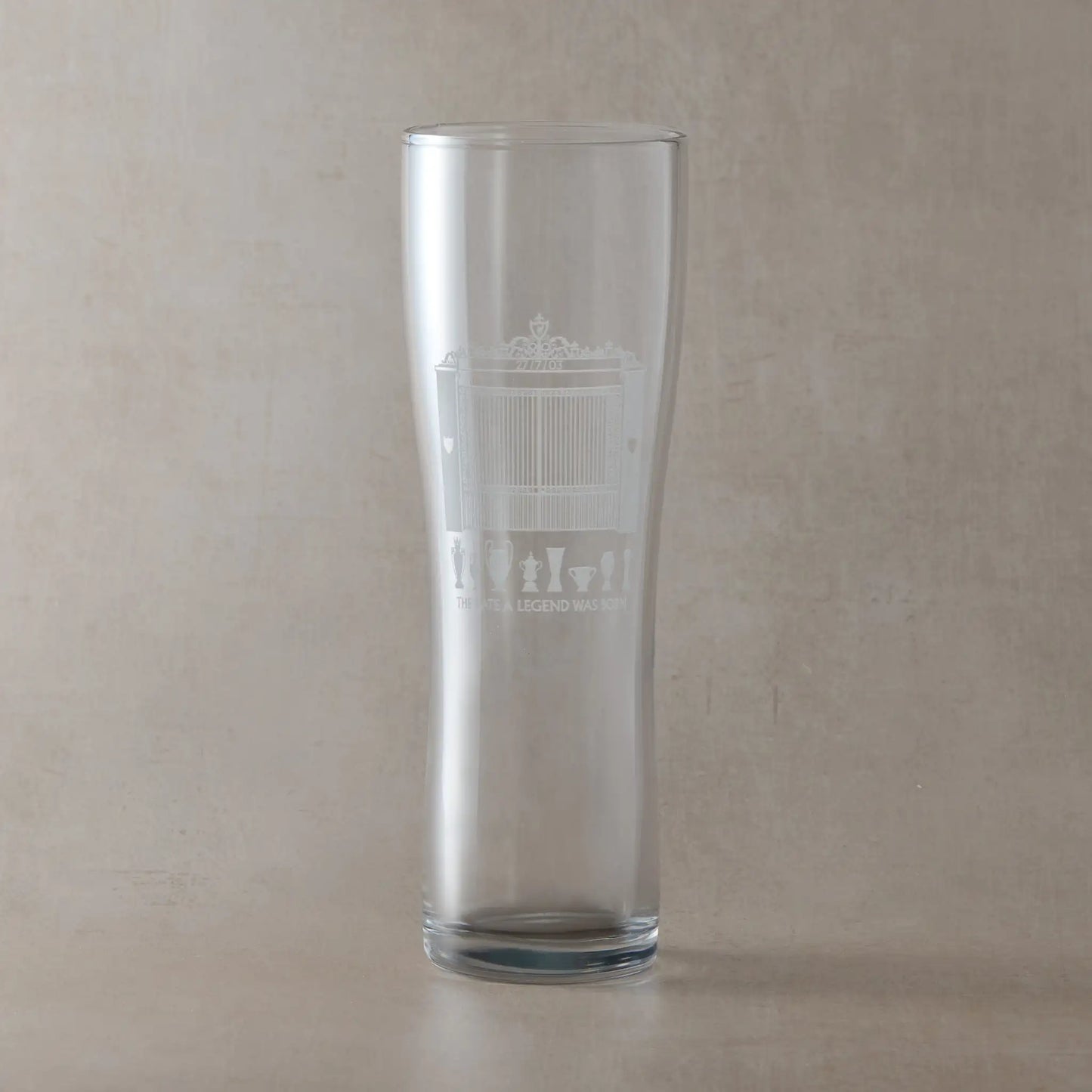 Personalised pint glass engraved with trophies and Anfield design on a beige background