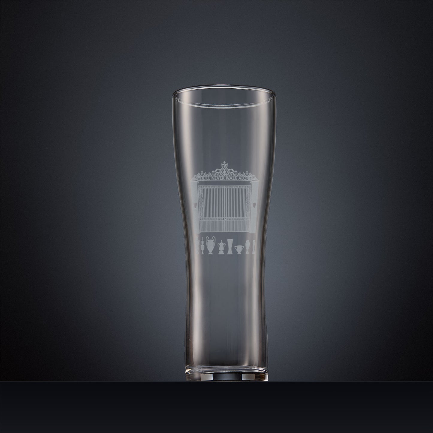 Engraved pint glass featuring the Shankly Gates and trophy silhouettes, shown here on a dark background to highlight the fine detail of the sandblasted engraving.