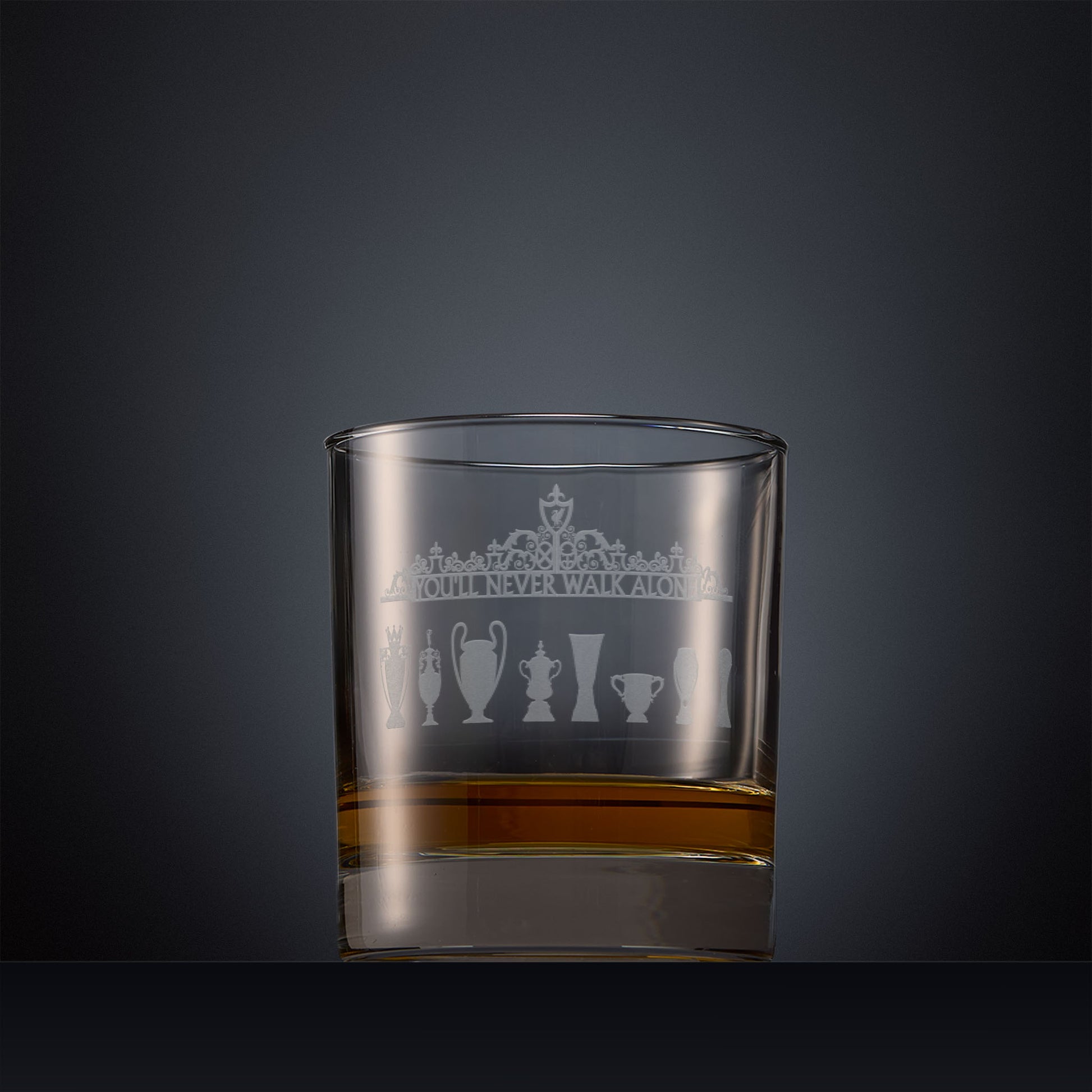 Engraved whisky glass featuring the Shankly Gates detail with trophy silhouettes, shown on a dark background to highlight the fine detail of the sandblasted engraving
