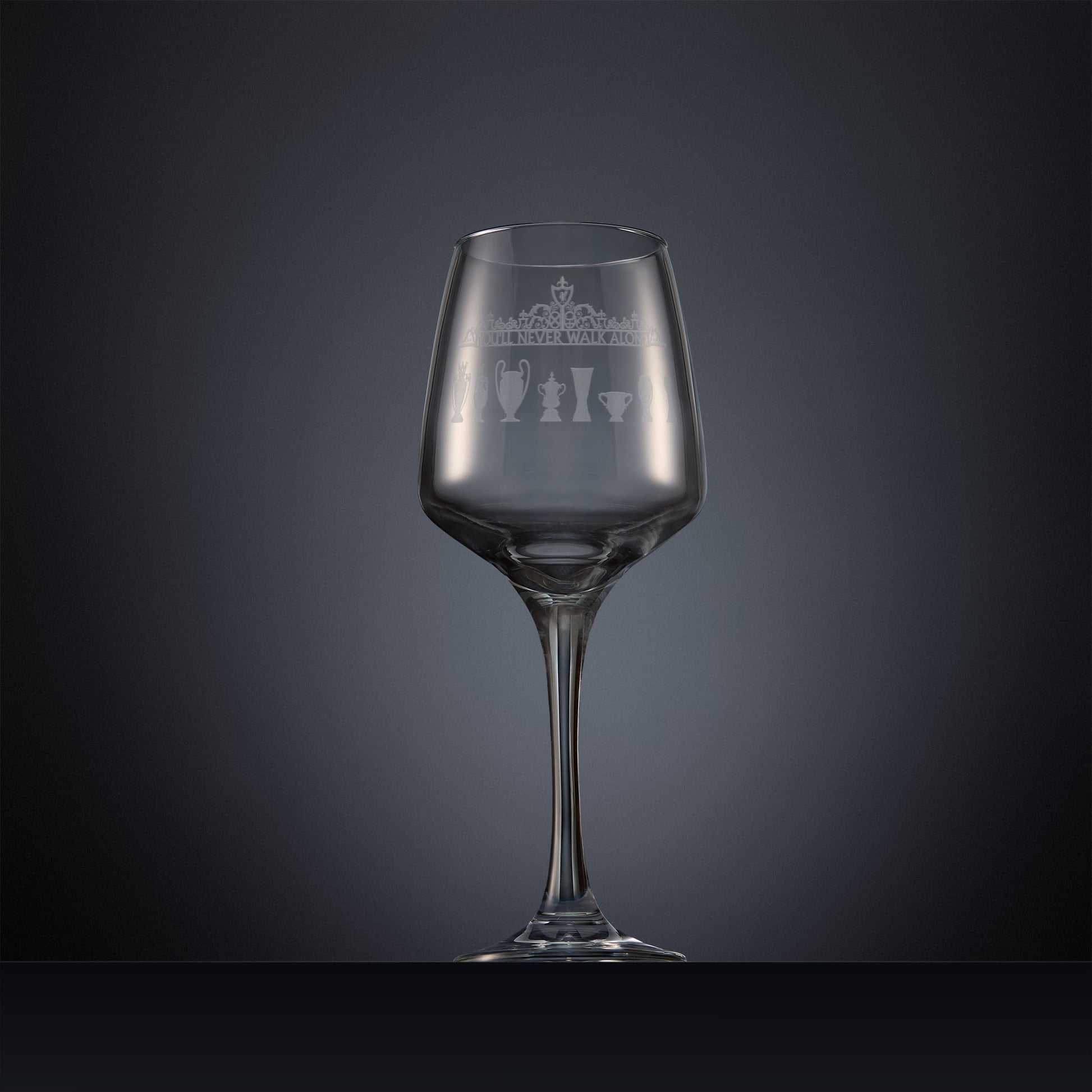 Engraved wine glass featuring the Shankly Gates overthrow with eight trophy silhouettes, shown on a dark background to highlight the fine detail of the sandblasted engraving