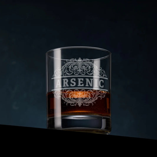 Whisky glass with 'Arsenic' etched on it, filled with a dark liquid against a dark background