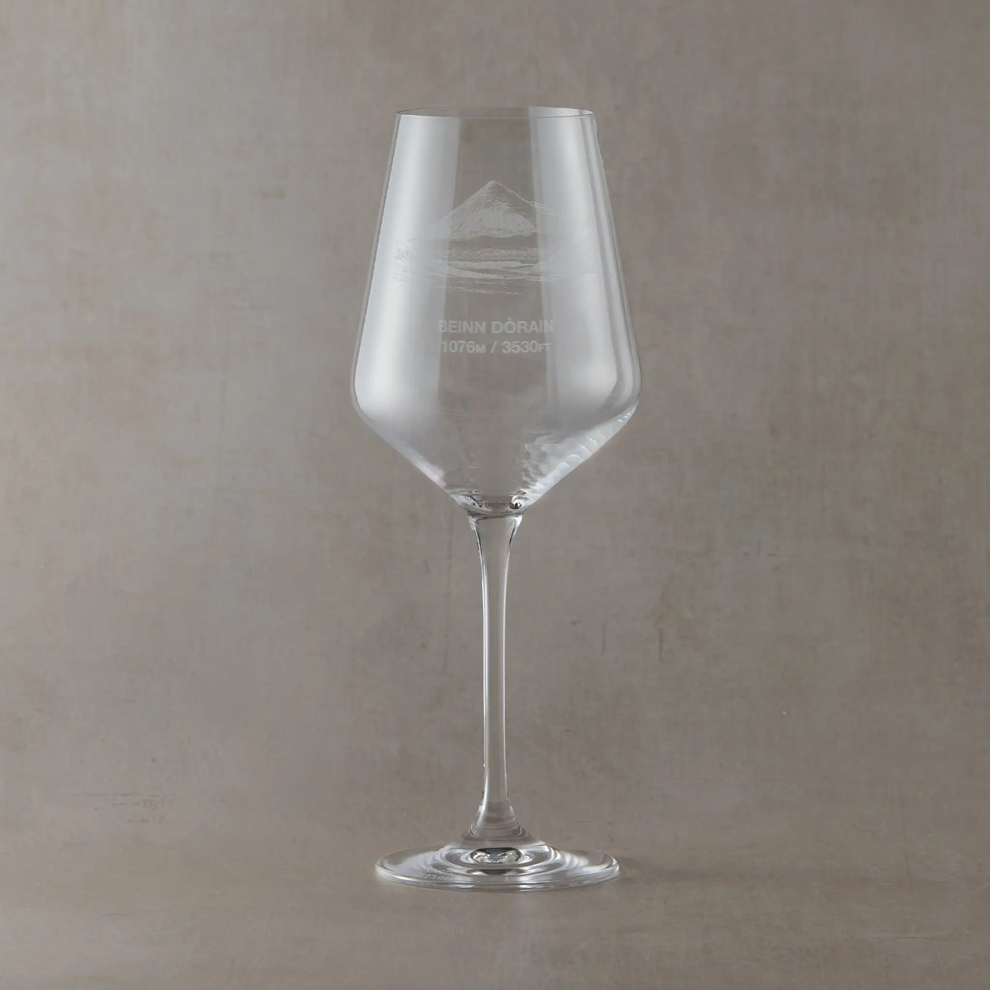 Clear wine glass with engraved Beinn Dorain mountain design on a beige background