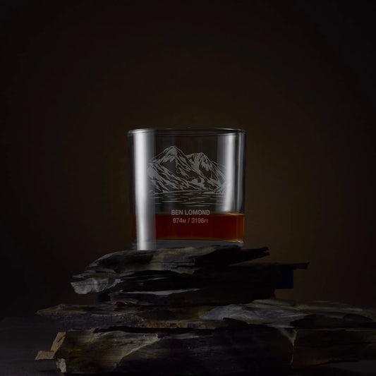 Whisky glass engraved with Ben Lomond and its height in metres on rocks against a dark background