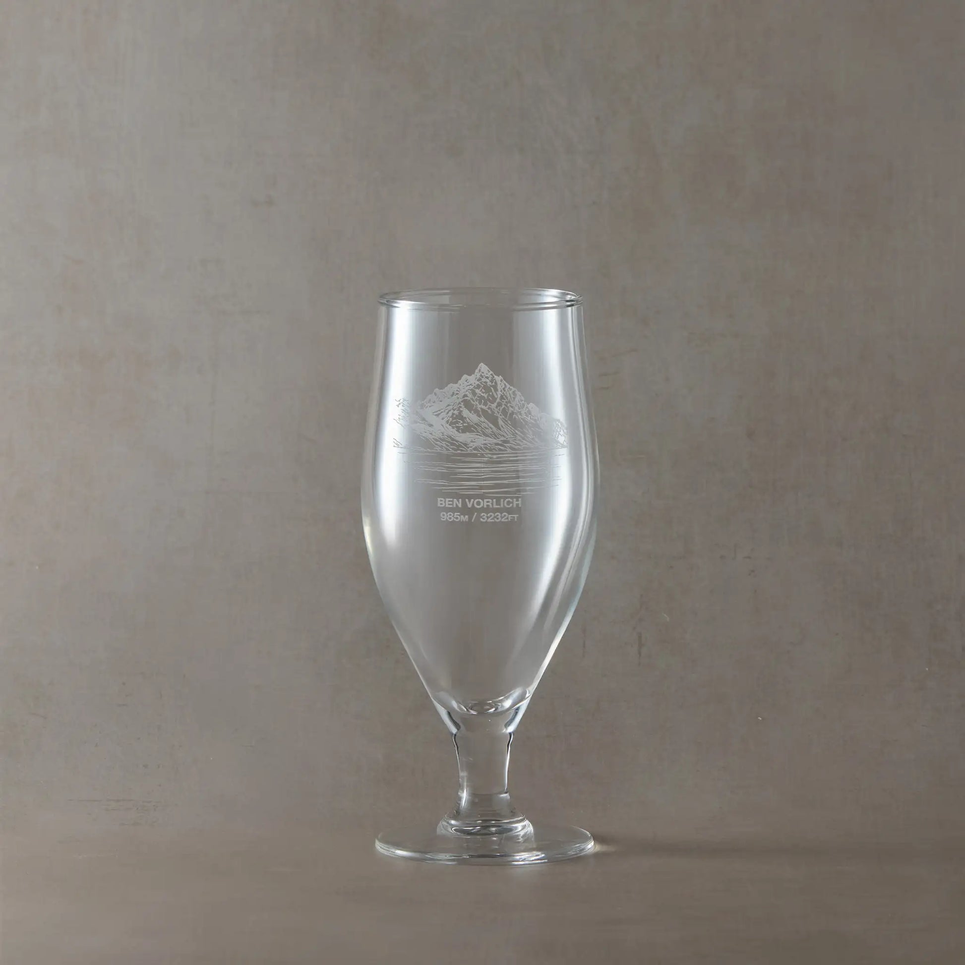 Clear beer glass with engraved design of Ben Vorlich on a beige background