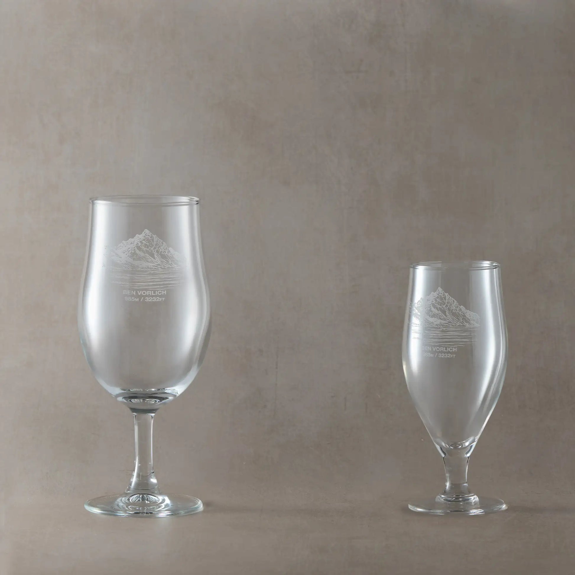 Two stemmed beer glasses with engraved Ben Vorlich mountain on a beige background