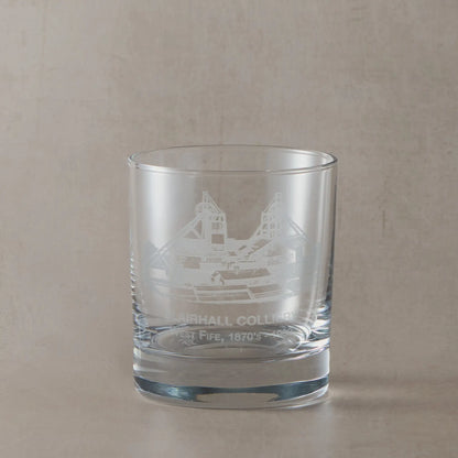 Glass of whiskey with ice featuring an engraved coal mine design on a dark background
