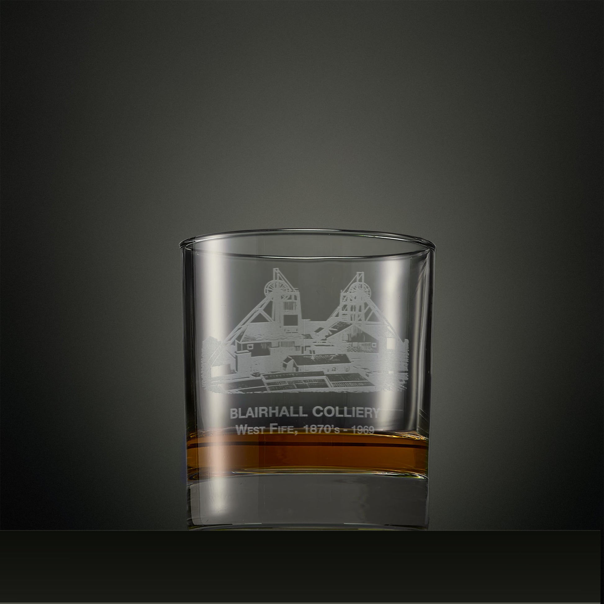 Clear glass tumbler with engraved coal mine design on a dark background