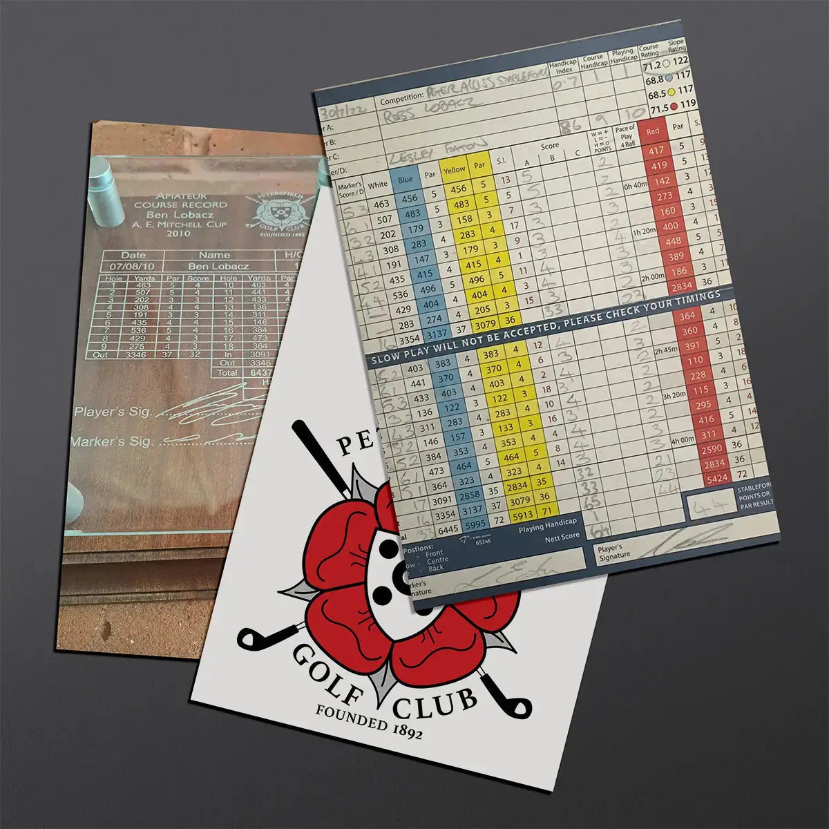 A set of golf-themed printed materials laid on a dark gray background: a transparent scorecard insert, a white card with a red rose and black golf club graphic.