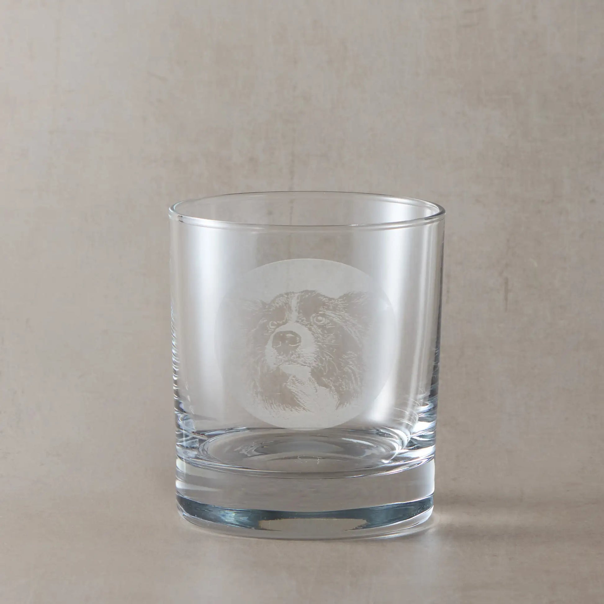 Whisky glass with engraved portrait of a Border Collie on a beige background