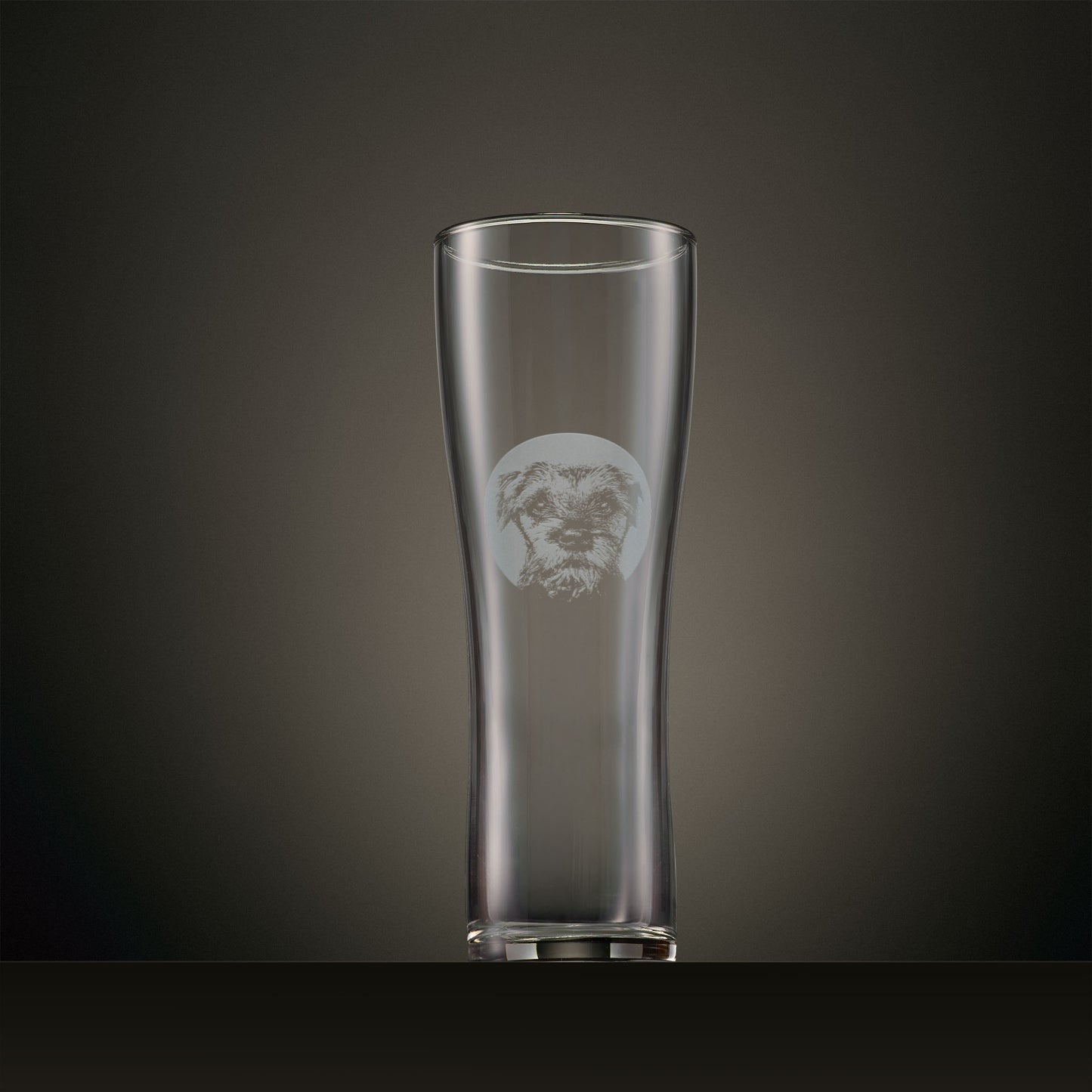 Engraved pint glass featuring a Border Terrier portrait set within a circular design, photographed on a dark studio background