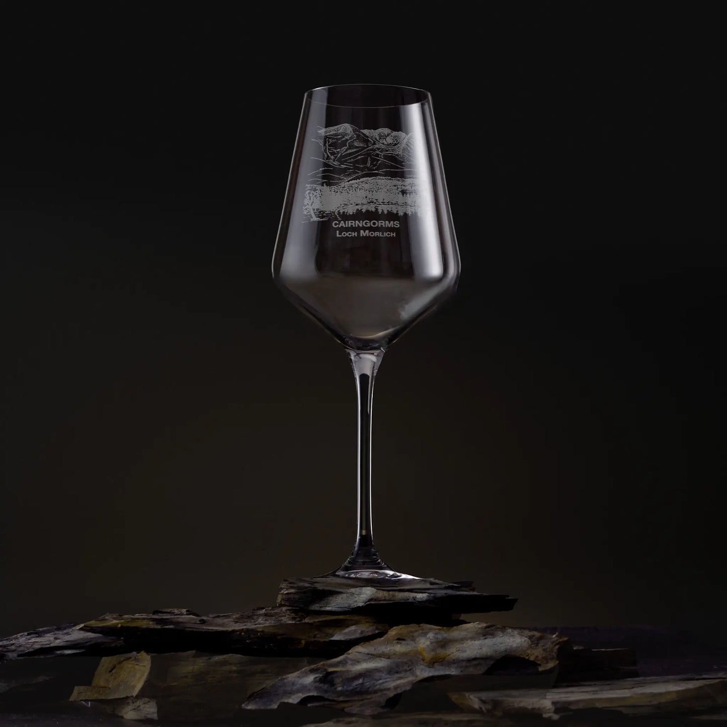 Engraved wine glass featuring the Cairngorms and Loch Morlich landscape, shown on a dark studio background with a detailed mountain and waterline design