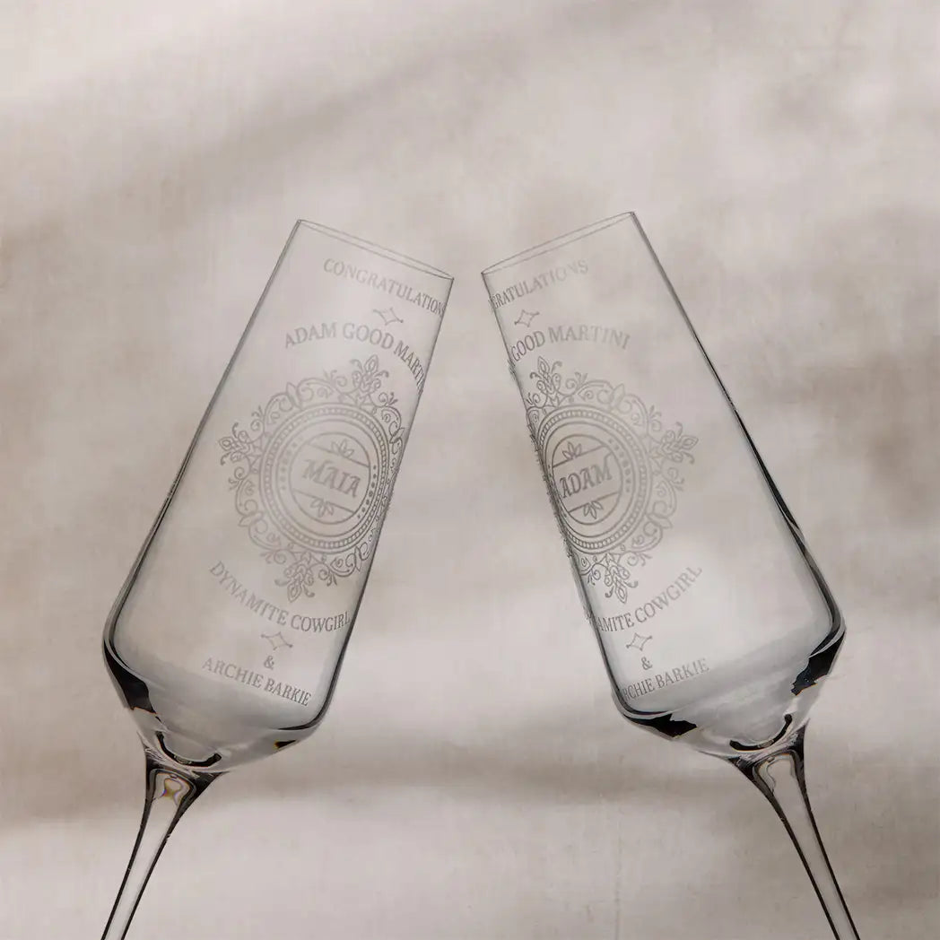 Two engraved champagne flutes on a textured surface