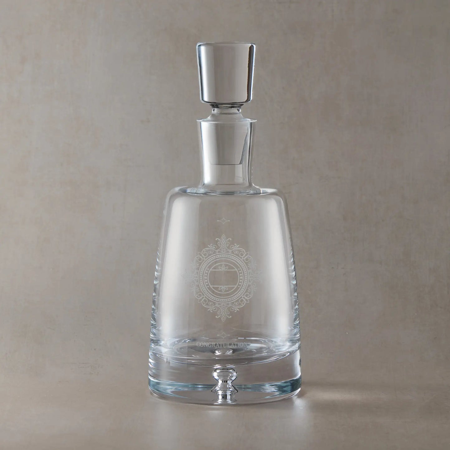 Clear glass decanter with engraved wedding anniversary design on a beige background