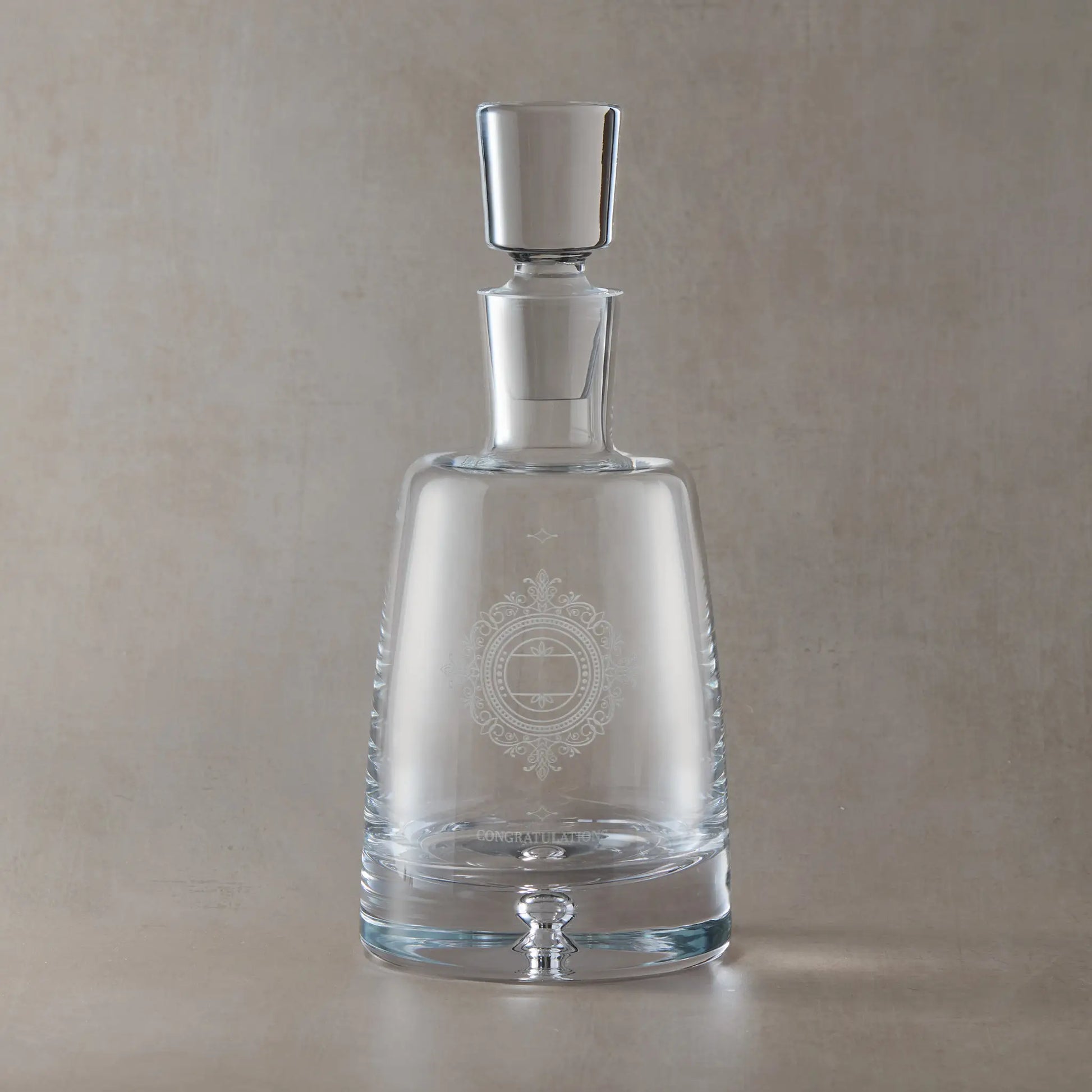 Clear glass decanter with engraved wedding anniversary design on a beige background