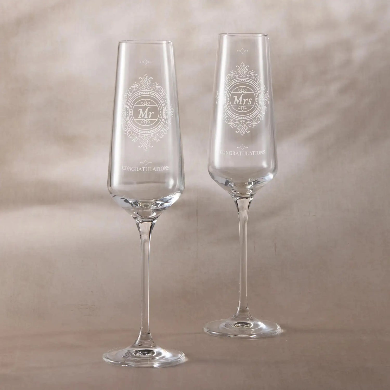 Two wedding champagne flutes with 'Mr' and 'Mrs' engravings on a beige background