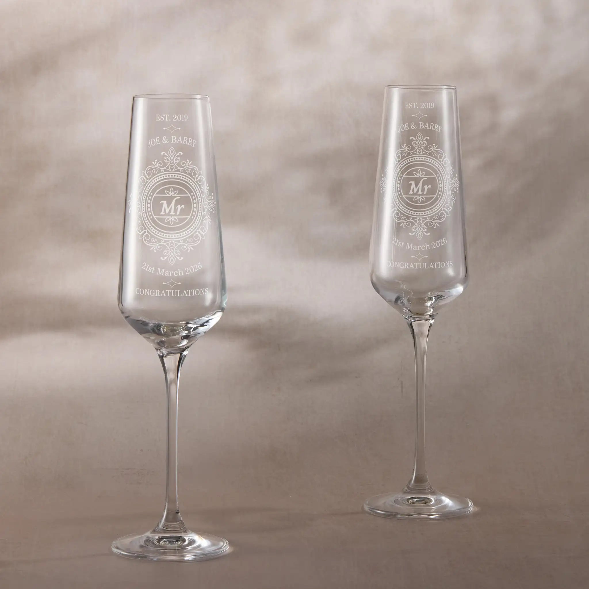 Chantilly lace engraved champagne flutes personalised for Mr and Mr, photographed on a neutral ivory background.