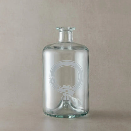 Engraved apothecary decanter featuring a Scottish clan crest with belt and buckle motif, centre left blank for your own design, set on a clear glass bottle against a neutral beige studio background
