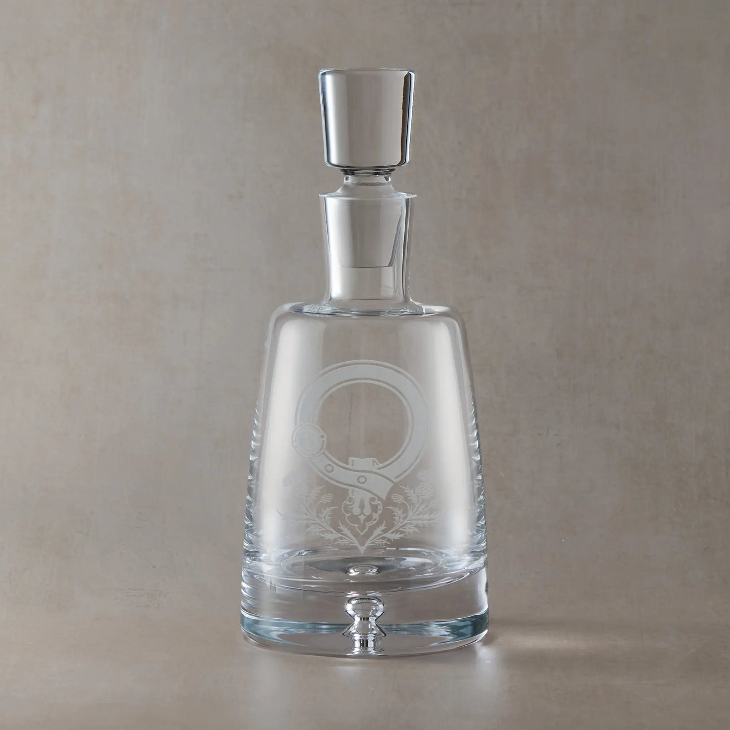 Handmade engraved decanter featuring a Scottish clan crest with thistles and central cartouche, left blank for your own family name, set against a neutral beige studio background
