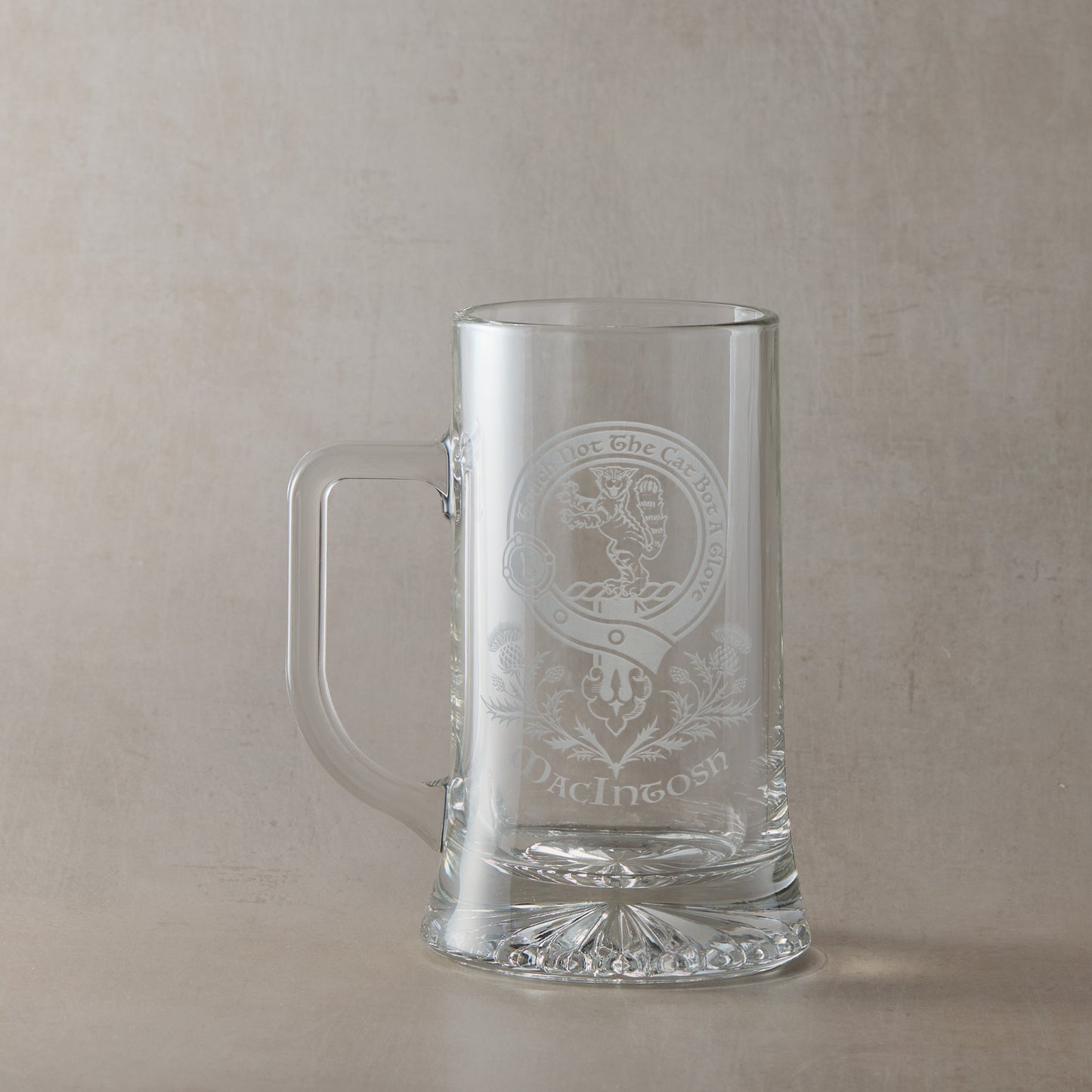 Clear glass tankard with engraved Scottish Clan Crest design and motto on a beige background