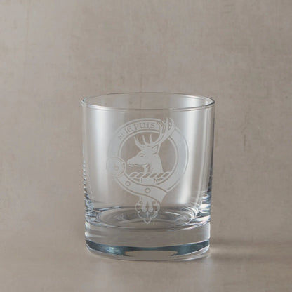 Engraved whisky glass featuring a Scottish clan crest with belt and buckle motif, sandblasted on a clear glass tumbler against a neutral beige studio background