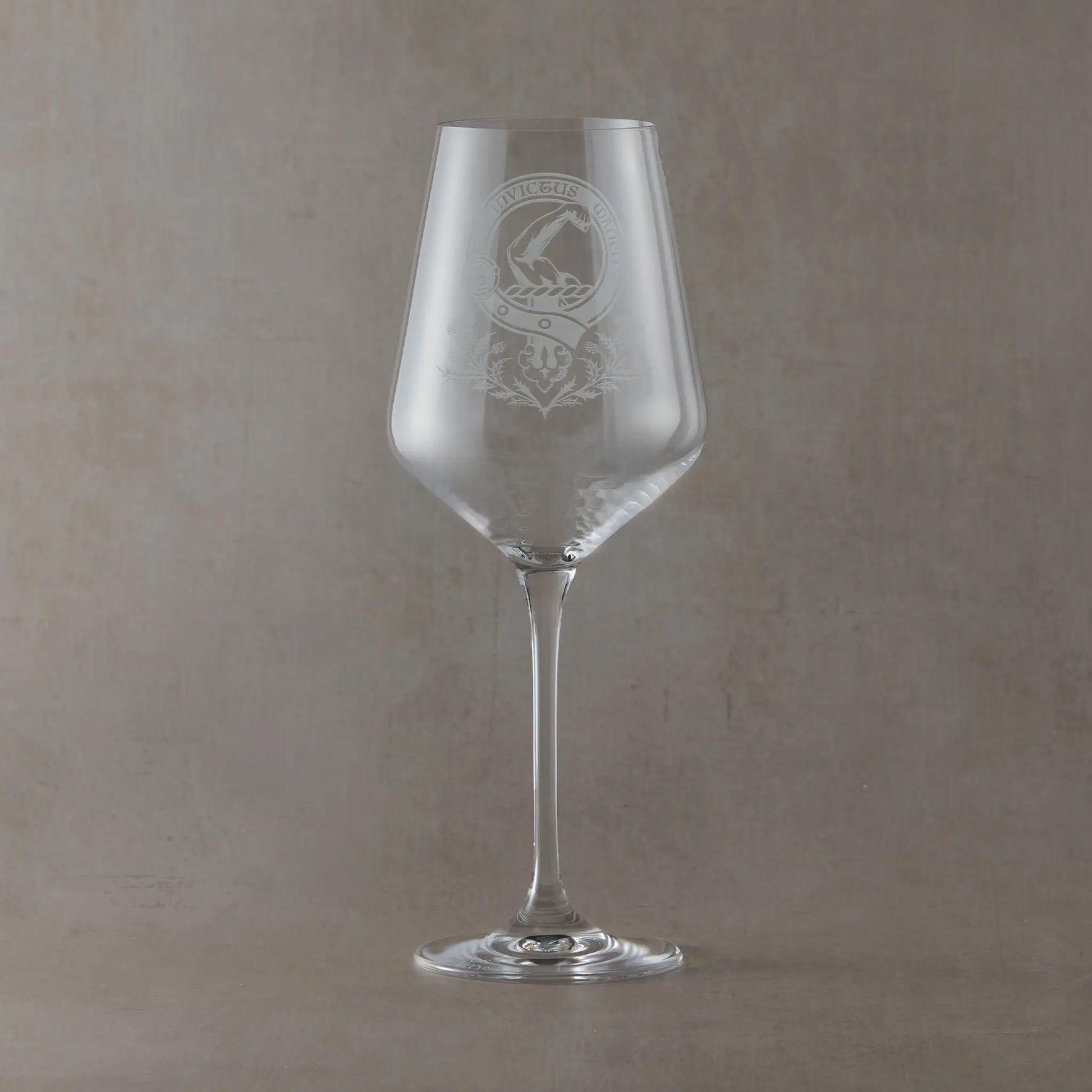 Engraved wine glass featuring a Scottish clan crest with belt and buckle motif, sandblasted on a clear Atelier wine glass against a neutral beige studio background
