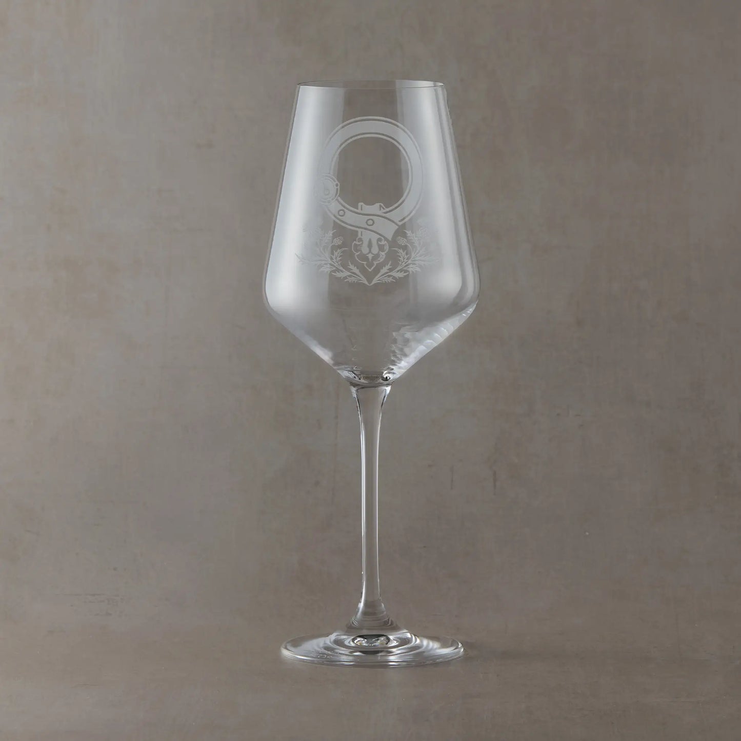 Wine glass with an engraved clan crest and thistle design on a grey background