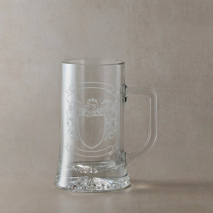 Engraved glass tankard featuring a heraldic coat of arms with a central shield left clear for your own design, handle on the right, set against a neutral beige studio background