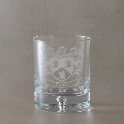 Whisky Engraved whisky glass featuring a heraldic coat of arms with mantel, shield and surname, sandblasted on a clear Atelier whisky glass against a neutral beige studio background