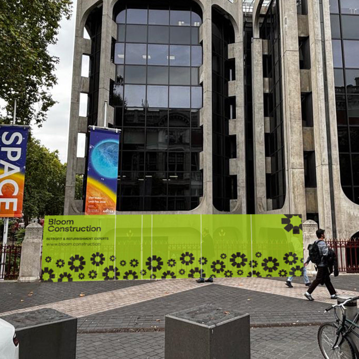 Green construction barrier with floral cog pattern in front of a large building