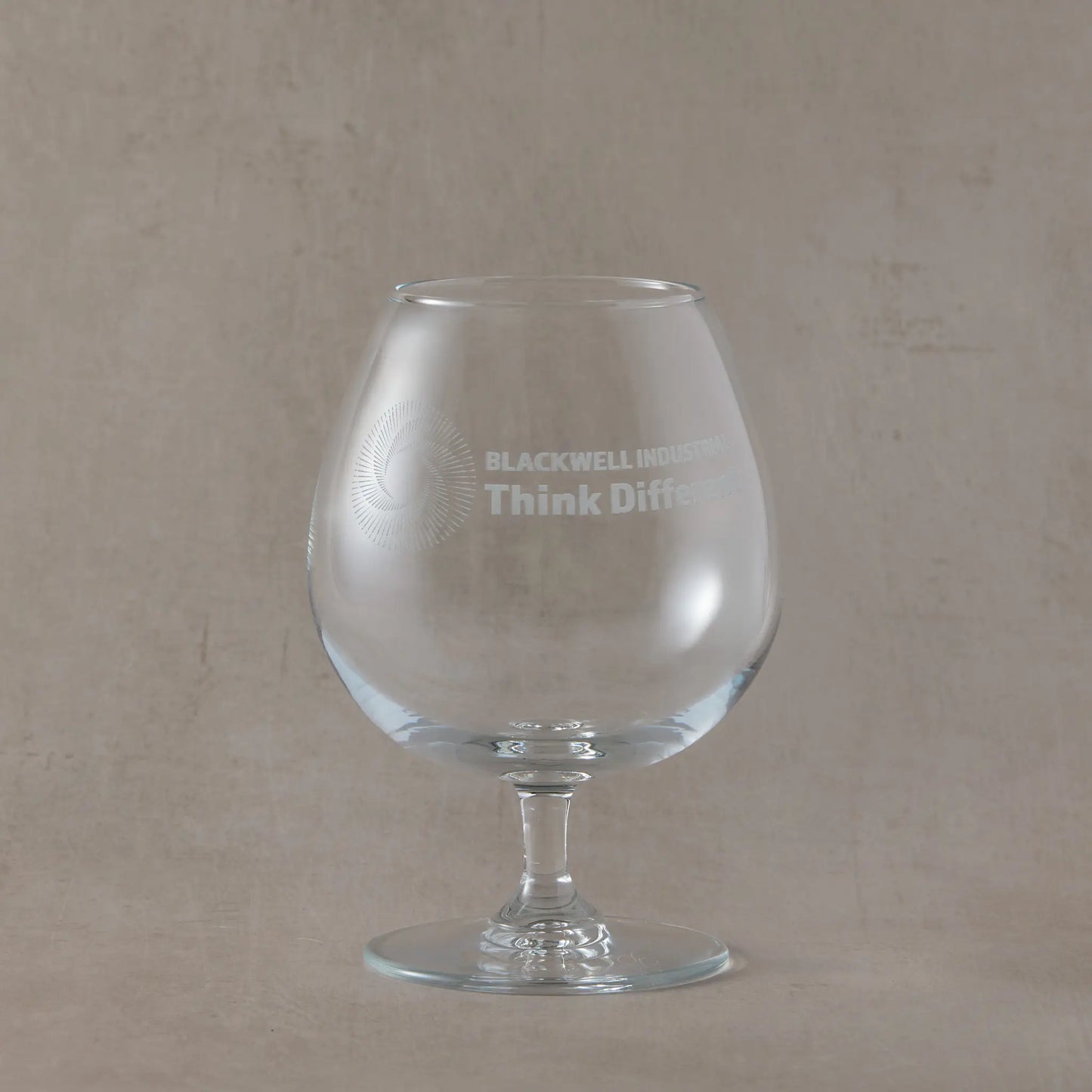 Clear brandy glass with engraved corporate logo and text on a beige background