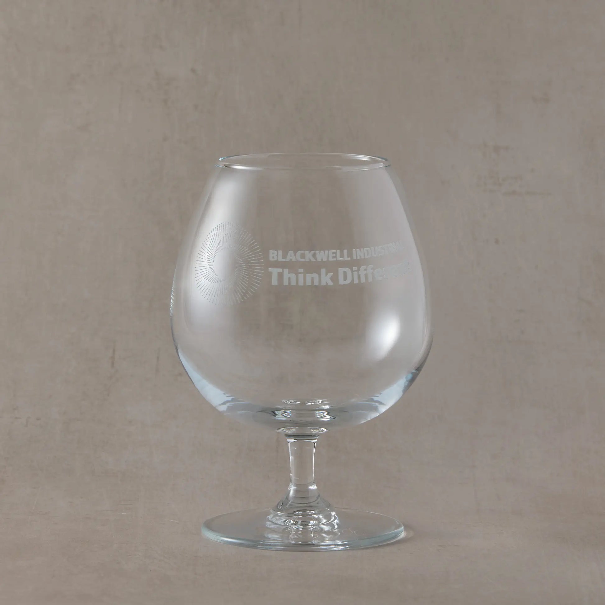 Clear brandy glass with engraved corporate logo and text on a beige background