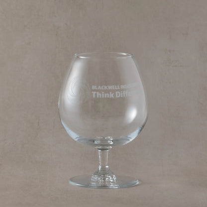 Clear brandy glass with engraved corporate logo and text on a beige background