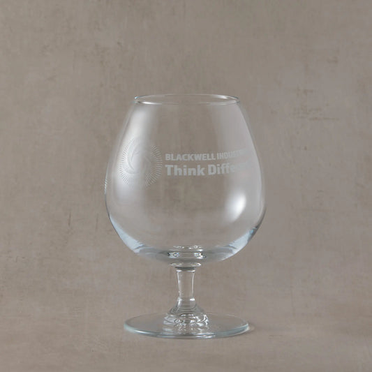 Clear brandy glass with engraved corporate logo and text on a beige background